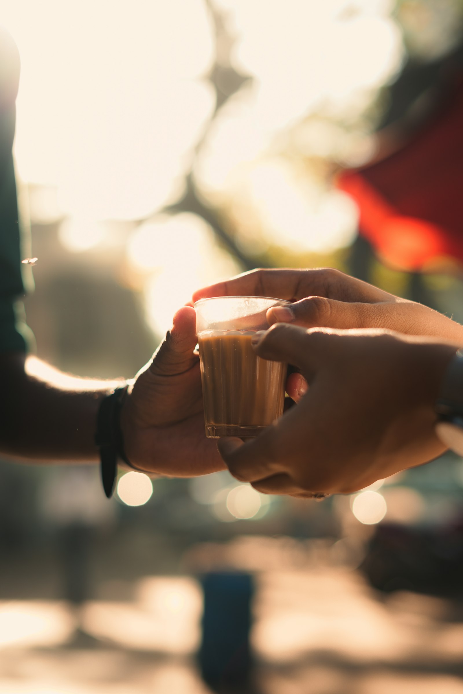 One hand passing a glass of chai to another in warm evening light
