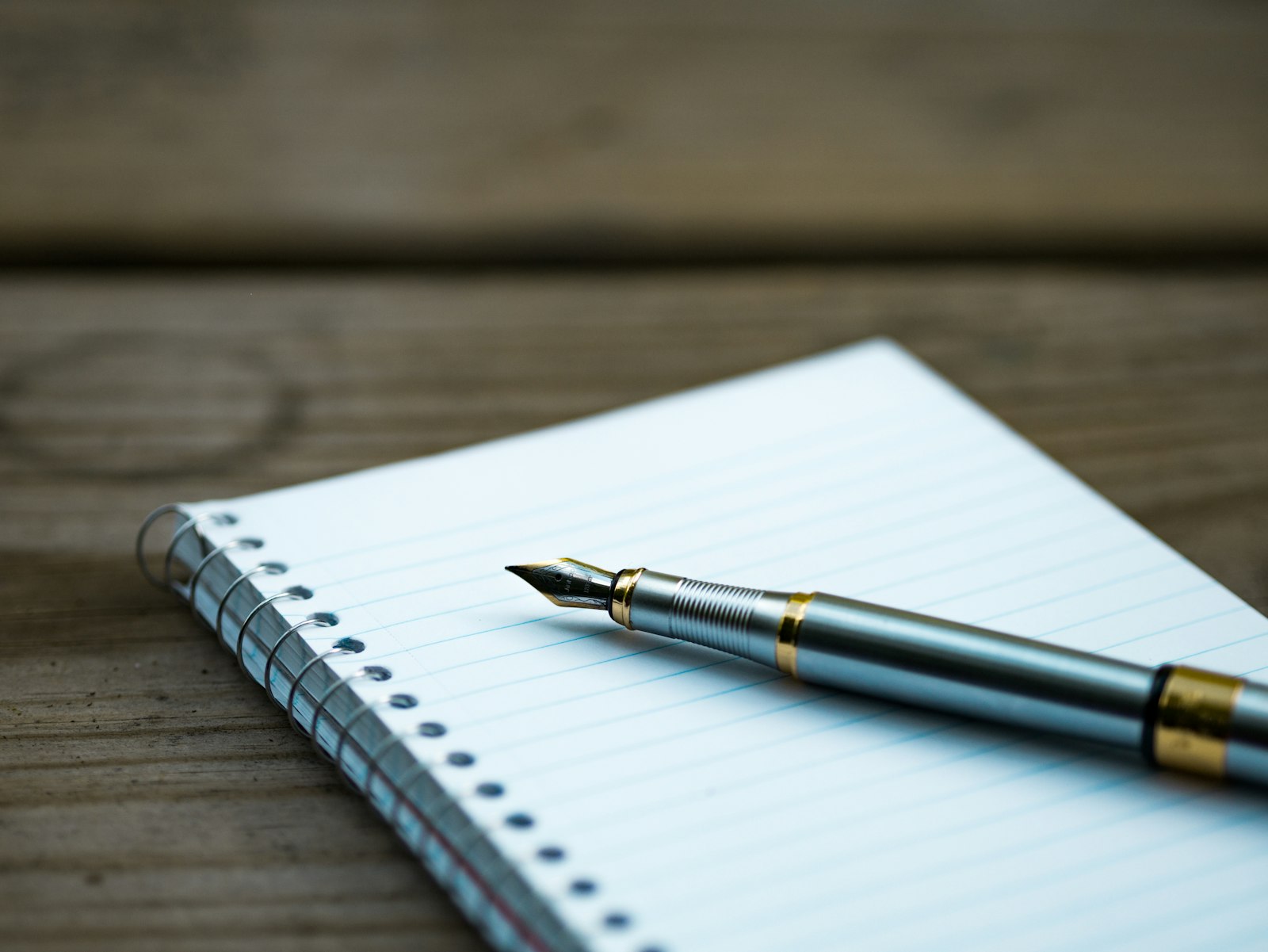 Fountain pen resting on an open ruled notebook on a wooden table