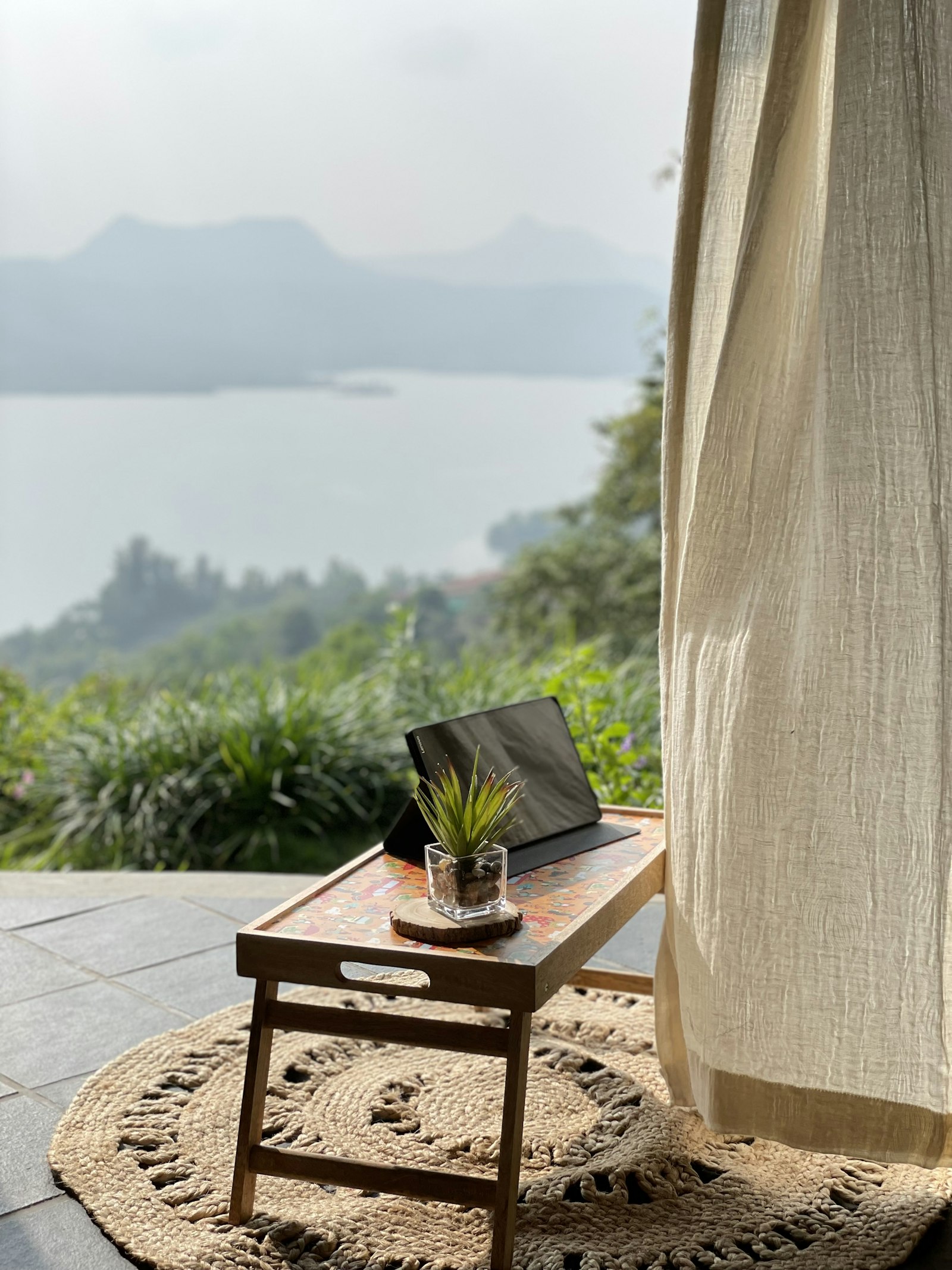 Laptop on a small wooden table on a veranda overlooking a lake and hills
